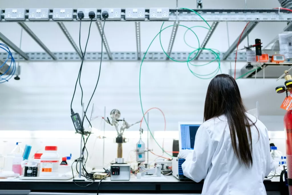 Pesquisadora em laboratório utilizando equipamentos científicos e analisando dados em um computador, representando o ambiente de inovação científica das deep techs.
